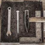 A collection of vintage workshop tools including a wrench, nail, and hammer displayed on a wooden table.